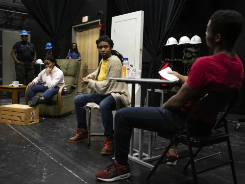 Actors dressed as auto workers sitting and standing