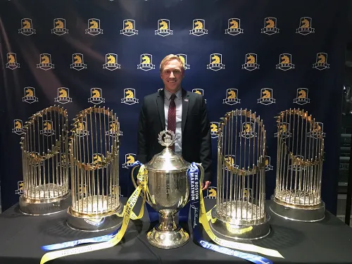 Man standing behind Boston Marathon trophy and world series trophies