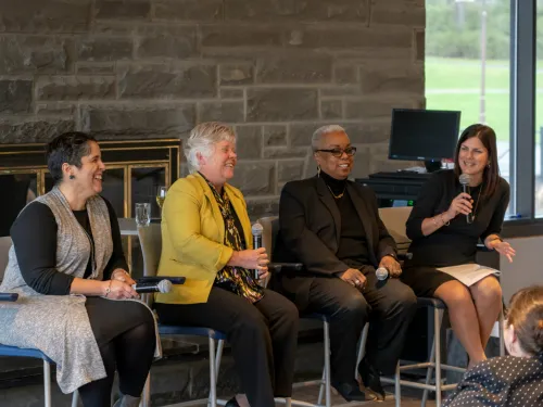 Four women speaking in front of a fireplace