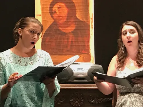 Two women singing with a painting behind them