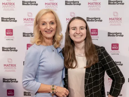 Two women pose in front of a backdrop