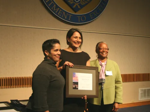 Three women posing with a plaque