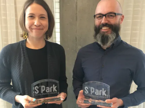 A man and a woman holding glass awards