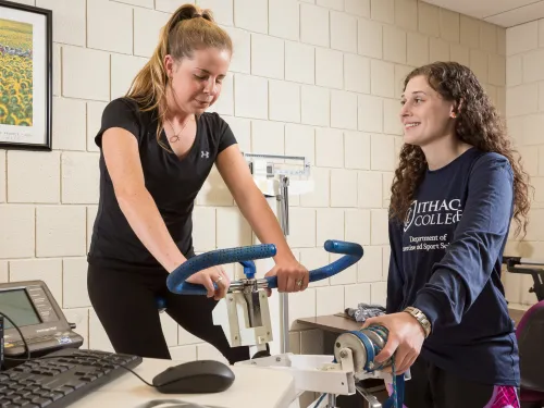 Two students perform a stationary bike test in a lab classroom.