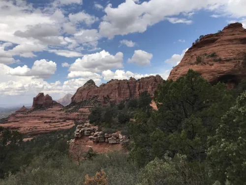 A sweeping view of a desert landscape, featuring shrubby vegetation and craggy red rocks and mountains.