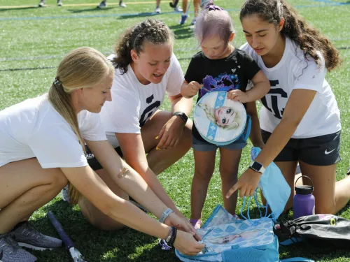 A toddler on an athletic field with a three young women