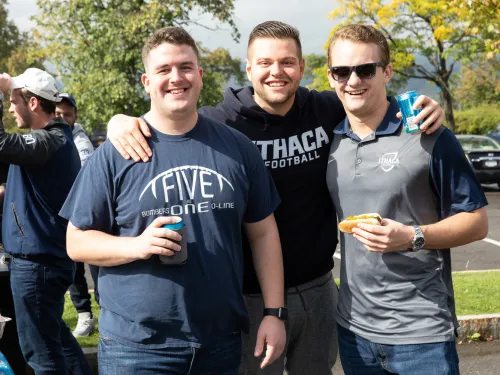 Three young men posing for a photo by a grill