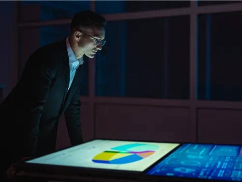 A man in a suit looks at graphs on a screen