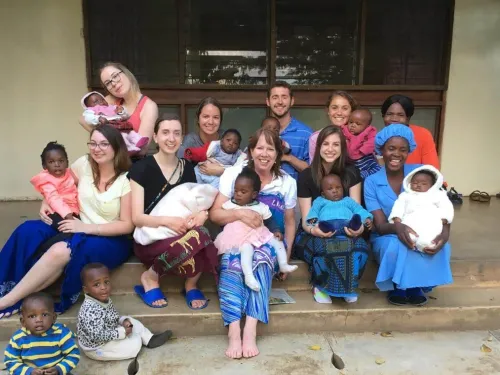 A group of students are seated on the steps with small children in front of a nursery in Malawi.
