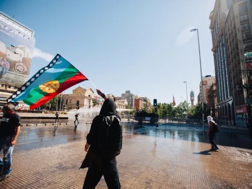 A blue, green, red and yellow flag being waved by a person in a public square