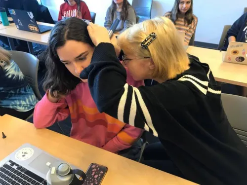 One student with a black shirt and blond hair is looking the ear of another student with an orange shirt and dark hair.