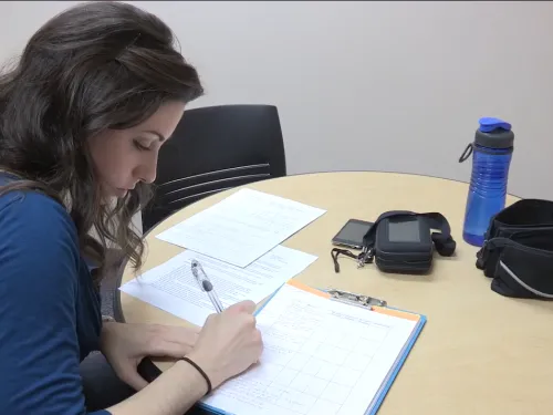 A student in a blue shirt and black hair is writing on a piece of paper.