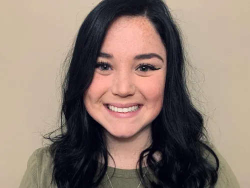 This is a photo of Casey Wrobel. Casey is wearing a short green shirt with a silver necklace. Casey's hair is long and black.