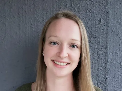 This is a photo of Courtney Yehl. Courtney is standing against a grey background. Courtney is wearing a long sleeve green shirt. 