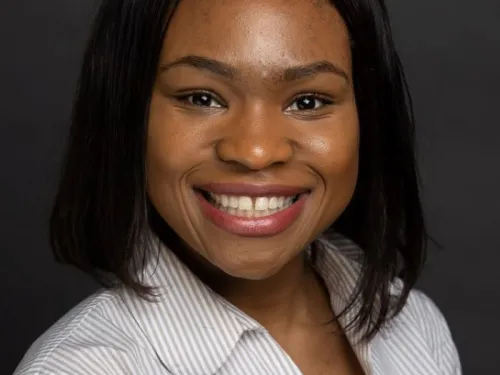 This is a photo of Efosa Erhunmwunse. Efos is wearing a white striped shirt and is smiling at the camera.