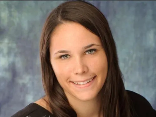 This is a photo of Tara Schoor. Tara is wearing a short sleeve black shirt and has long dark hair. The photo background is a gray color.