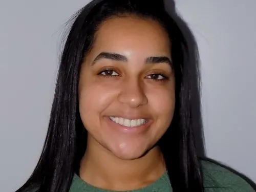 This is a photo of Taylor Larkin. Taylor is smiling at the camera with long black hair over the shoulders. Taylor is wearing a long sleeve green shirt.