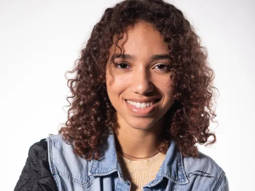 a young woman with curly brown hair smiling in a denim top