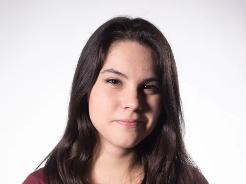 A young woman in a violet top with long brown hair.