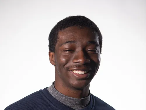 a yound man smiling with a navy blue top on and dark black hair.