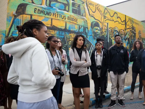 a group of MLK scholars stand in front of a colorful mural as they listen to their tour guide.
