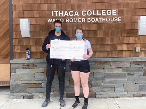 people holding a big check in front of a boathouse