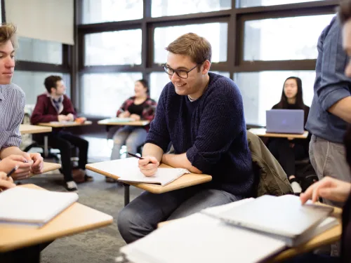Students sitting at their desks in a circle formation talking.
