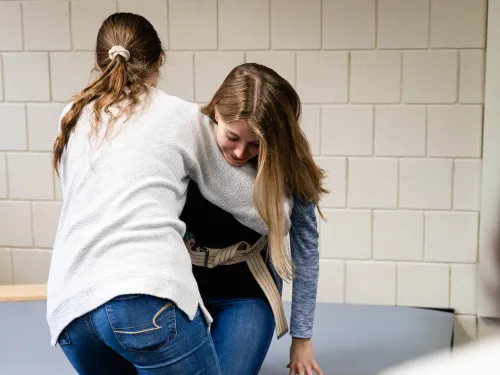 A student is providing assistance to another student with sitting down.