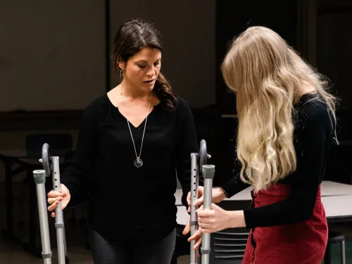 A faculty member is holding a walker and providing instruction to a student with long blond hair.