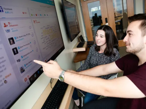 Two students are seated in front of a computer screen analyzing data.