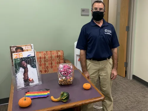 Luca Maurer standing in front of a table with safe space stickers, pronoun pins, and magazines