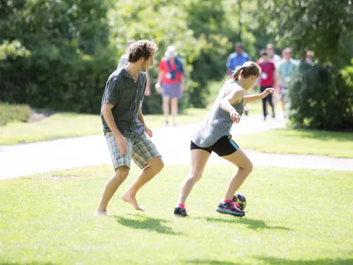Two students are playing soccer on a field together.