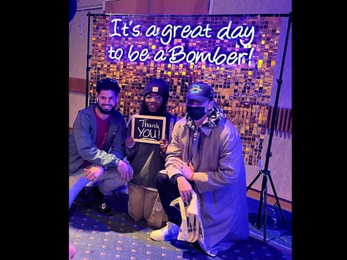 Students posing in front of a sign saying it's a great day to be a Bomber