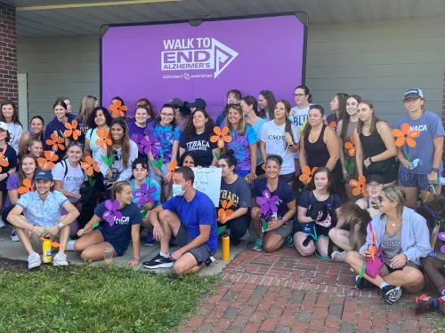 A group of IC students sitting outside in front of a sign that says Walk to End Alzheimers
