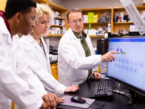 Two students working with a professor in a lab.
