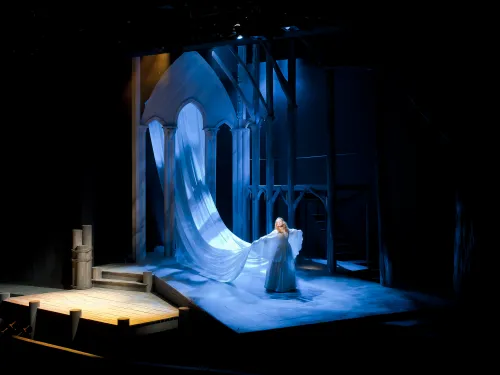 An actor downstage with a long flowing cape behind them going up to a church cathedral.