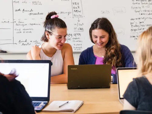 2 students sitting in front of white board looking at laptop