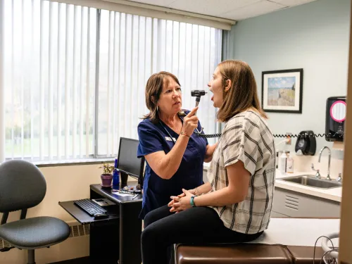 A female medical practitioner checks the tonsils of a female student