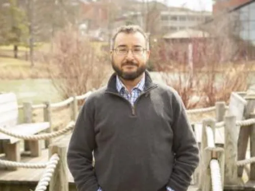 a man standing in front of a pond with a quarter zip jacket and jeans