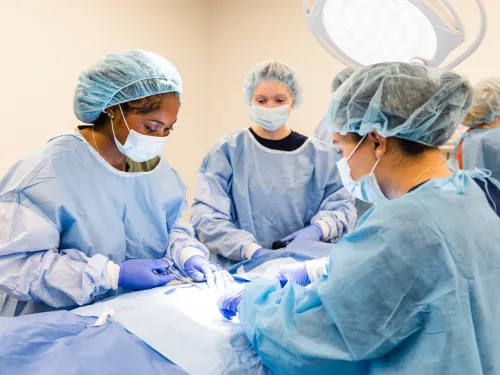 students in surgical caps and gowns provide care to a mannequin