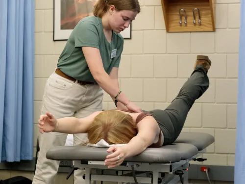 A student physical therapist is providing therapy to a theatre student on a table.