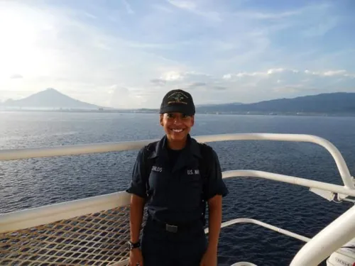 A woman in a US Navy uniform stands on the deck of a Naval vessel. 