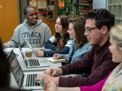 A group of students with laptops sit around a table 