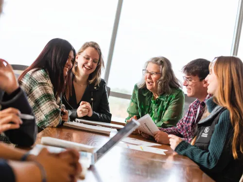 Smiling and laughing students gather around a professor. 