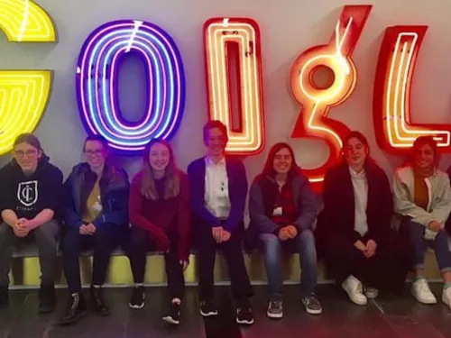 a group of students sits in front of a lit sign that spells out Google