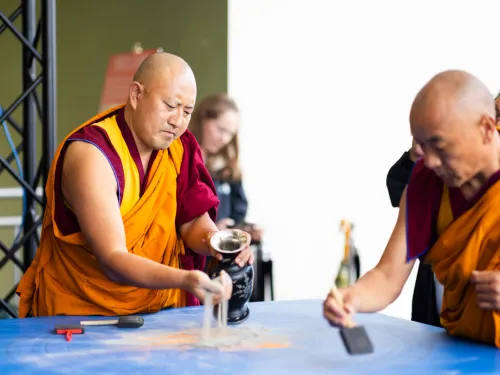 two monks pick up sand from a blue table 