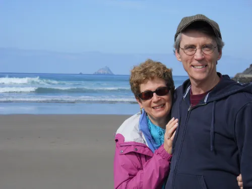 A smiling retired man and woman take a selfie at the beach. 