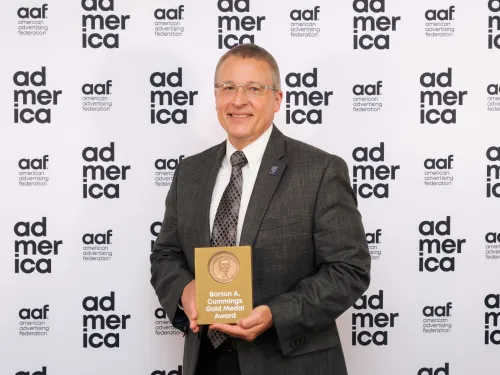 Man holding plaque standing on front of step-and-repeat screen.