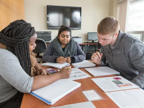 a peer tutor works with two other students at a table filled with books