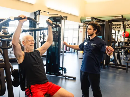 A student trainer helps a 65+ community member in a fitness facility.